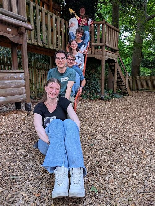 7 Personen sitzen auf einer Rutsche hintereinander.